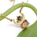 Crescent moon necklace in yellow gold with orange sapphire and salt and pepper diamond on a green stem