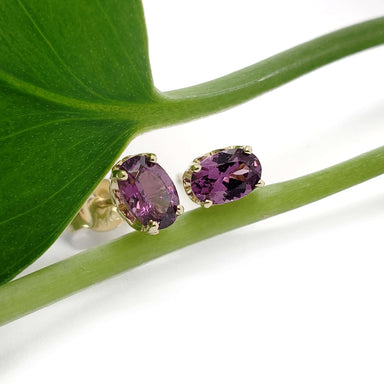 14kt yellow gold oval violet garnet stud earrings displayed on a green leaf