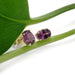 14kt yellow gold oval violet garnet stud earrings displayed on a green leaf