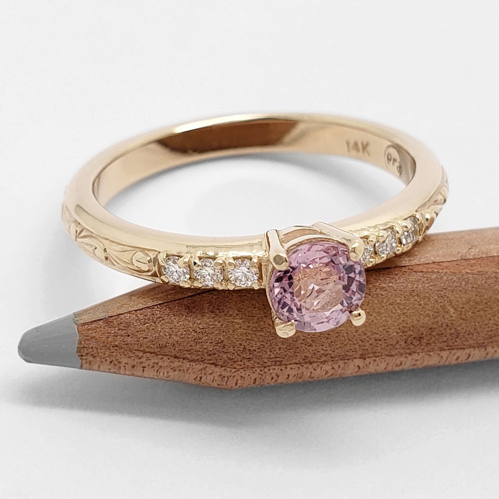 Yellow gold pink sapphire engagement ring with side diamonds, resting on pencil