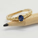 Yellow gold ring with blue sapphire and wheat pattern, displayed on a pencil