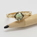 Yellow gold ring with green sapphire and floral motif, displayed on a pencil