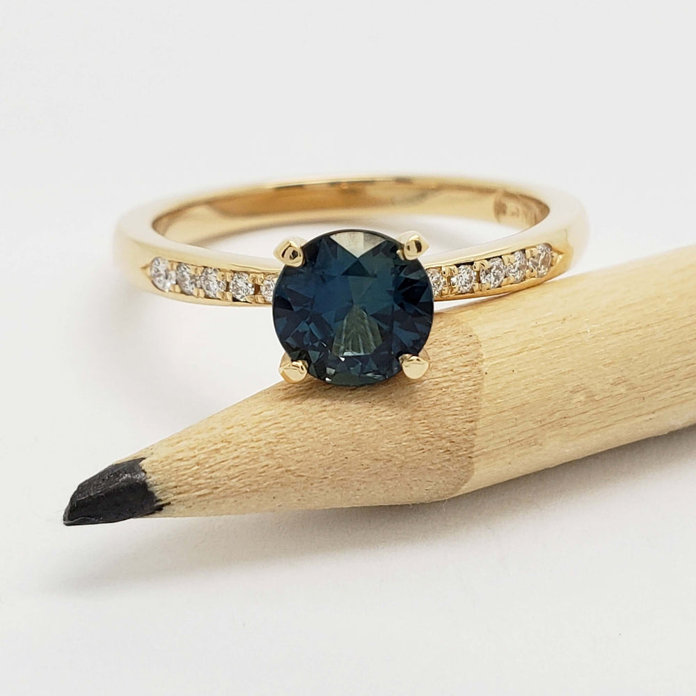 Round teal Australian sapphire and diamond ring in yellow gold, shown with pencil for scale