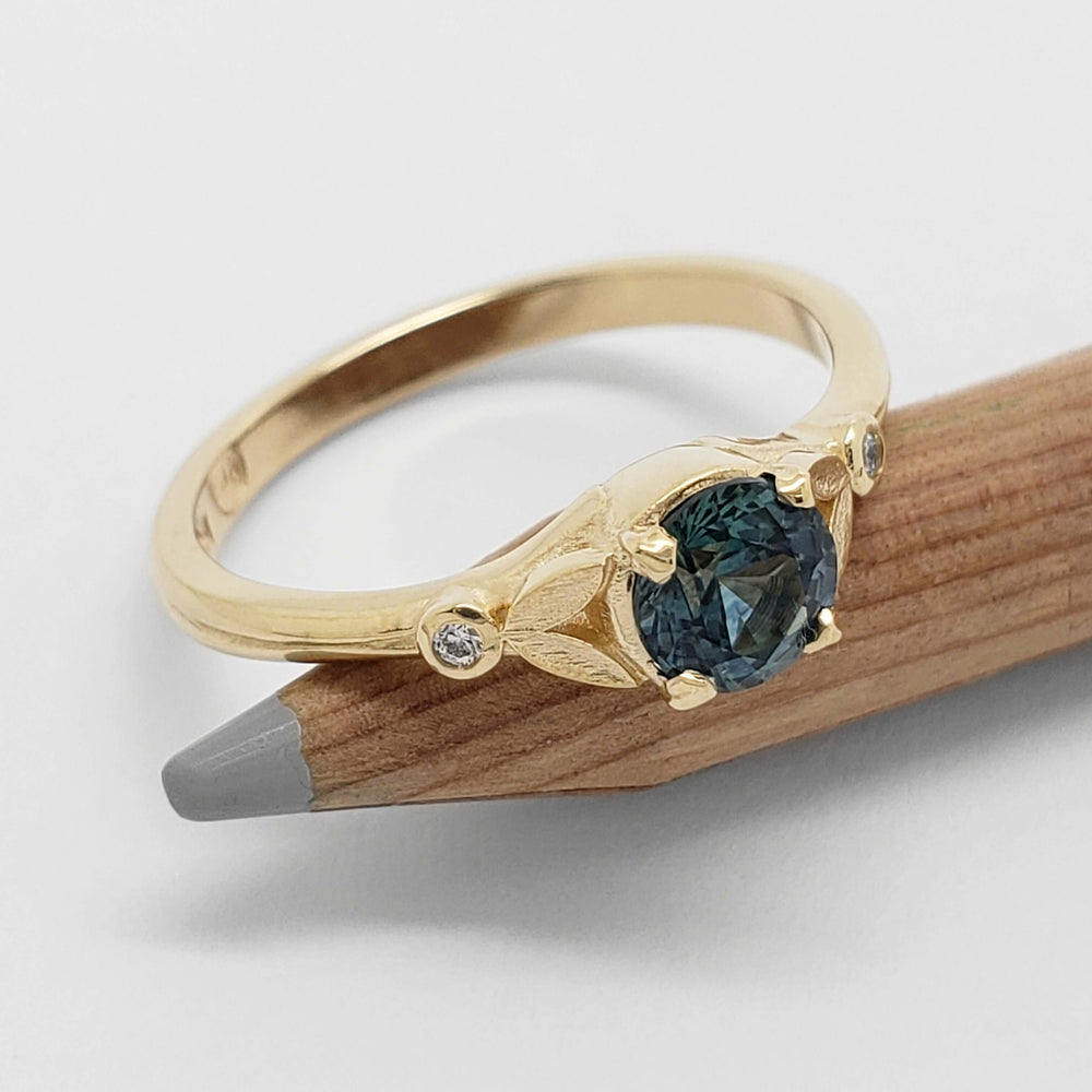 Yellow gold ring with teal Montana sapphire and bezel-set Canadian diamonds on a pencil
