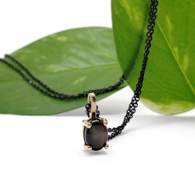 Star sapphire pendant in yellow gold with black chain, displayed against green leaves