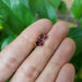Hand holding 14kt yellow gold oval violet garnet stud earrings outdoors