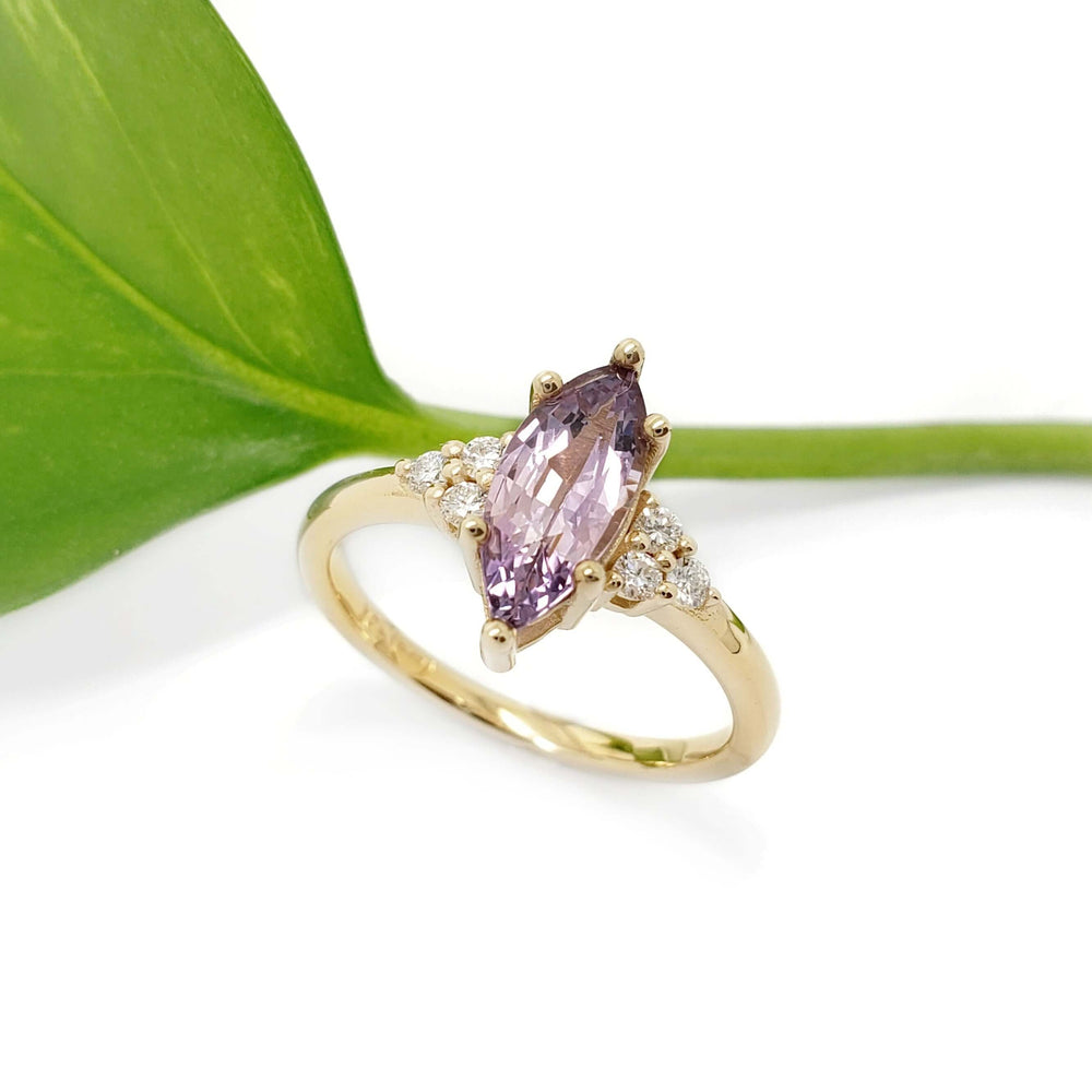 Zira ring with marquise purple sapphire and diamonds beside a green leaf