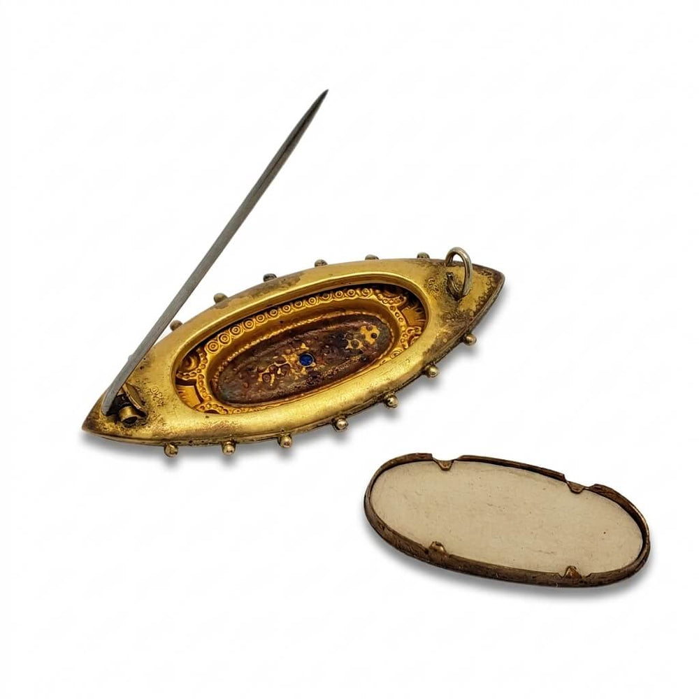 An antique gold-toned oval pin or brooch with a pin extending from the back, shown open next to its detached back cover on a plain white background.